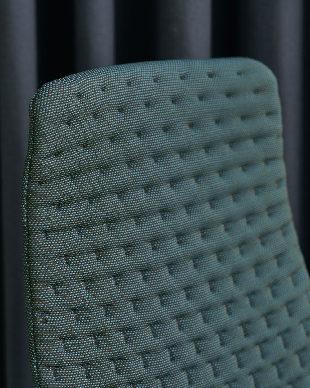 Nahaufnahme einer strukturierten Rückenlehne eines ergonomischen Bürostuhls vor einem dunklen Hintergrund.