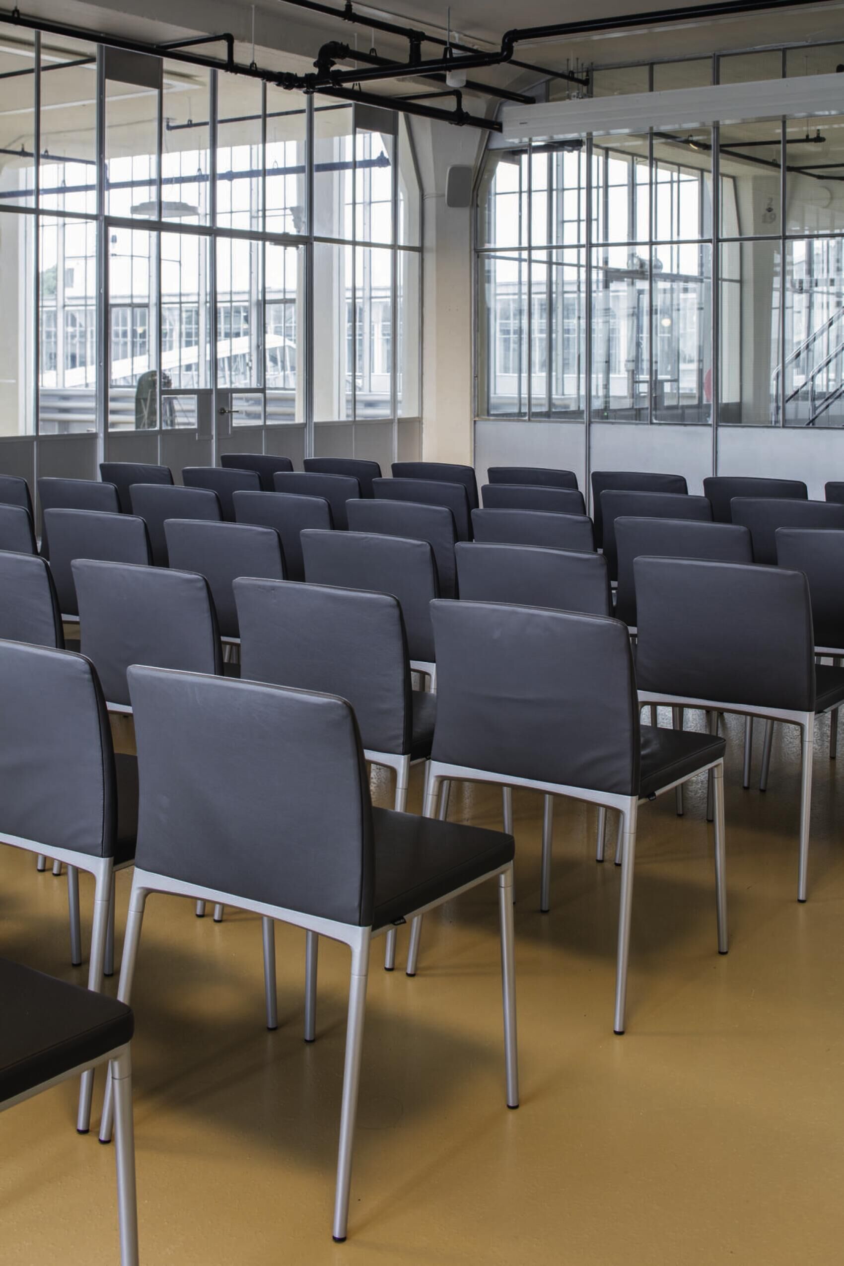 Reihe von modernen schwarzen Stühlen in einem lichtdurchfluteten Raum mit großen Fenstern und industriellem Design.