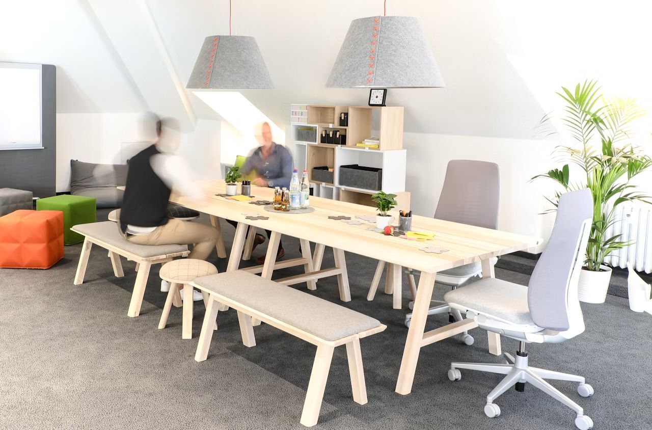 Moderner Büroraum mit ergonomischen Stühlen, großem Tisch und Pflanzen, fördert dynamisches und gesundes Sitzen.