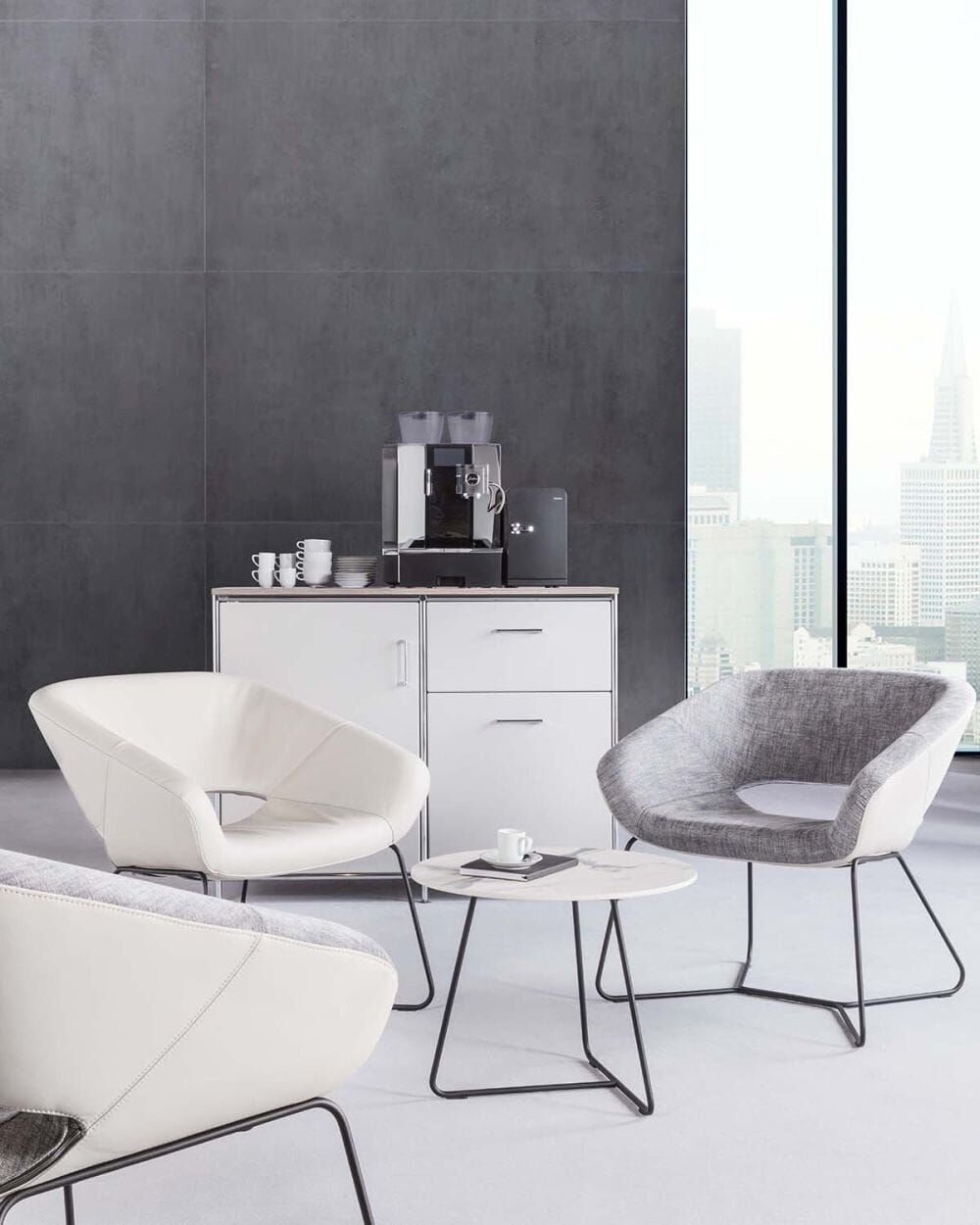 Moderne Lounge mit ergonomischen Stühlen, kleinem Tisch, Kaffeemaschine auf Schrank vor großem Fenster.