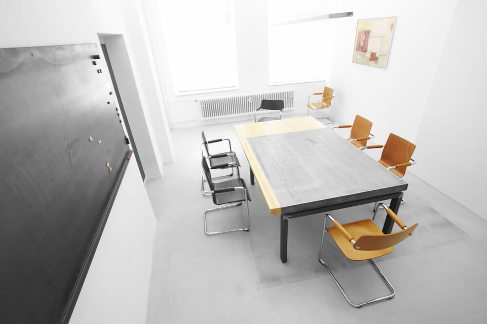 Moderner Konferenzraum mit ergonomischen Stühlen um einen großen Tisch, neben einer Schreibtafel an der Wand.