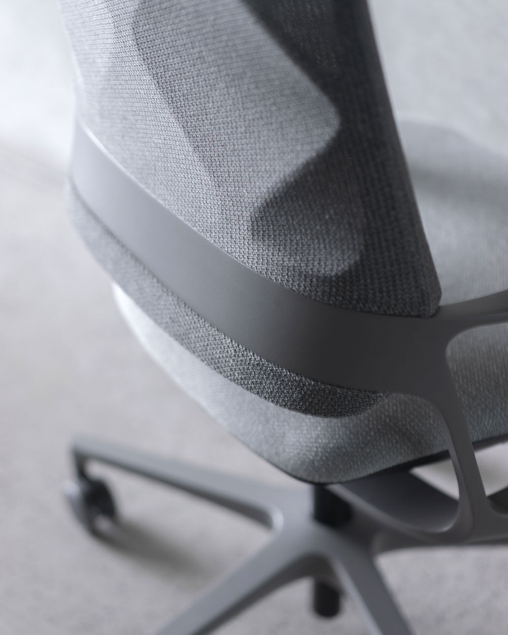 Nahaufnahme eines grauen ergonomischen Bürostuhls mit gewebter Rückenlehne und stabilem Drehgestell.