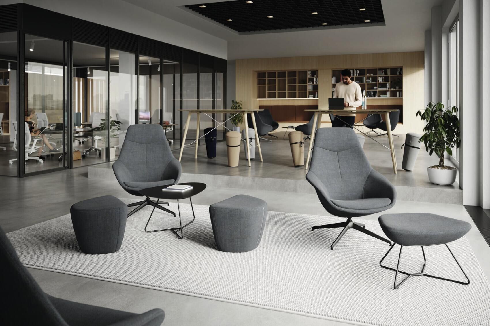 Moderne Bürolounge mit ergonomischen Sesseln, höhenverstellbarem Tisch und Glaswänden für eine offene und gesunde Arbeitsumgebung.