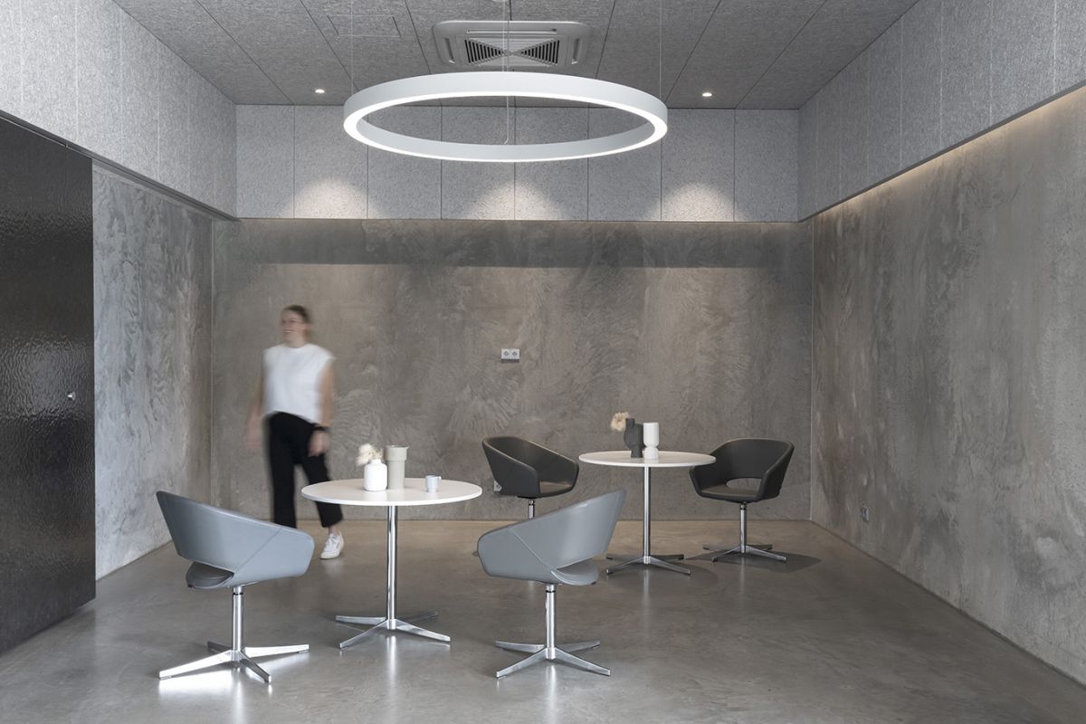 Moderner Besprechungsraum mit stilvollen grauen Stühlen, runden Tischen und einer Person im Hintergrund.