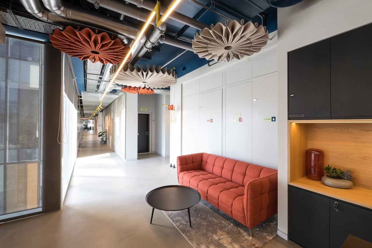 Moderner Büroflur mit gemütlichem roten Sofa, rundem Tisch und dekorativen Deckeninstallationen.