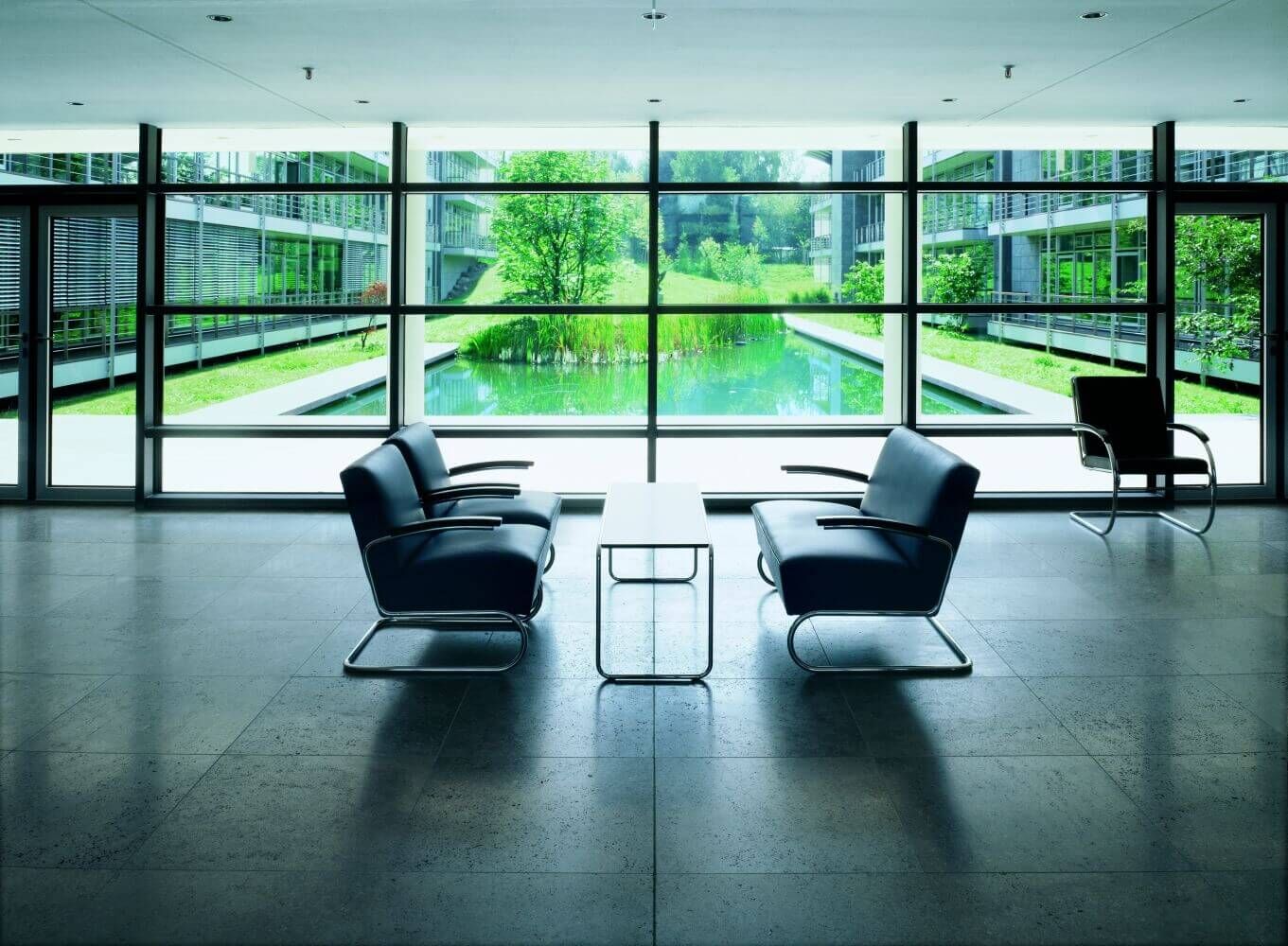Moderne Lobby mit Glasfront, hochwertigen schwarzen Stühlen und Blick auf einen grünen Innenhof mit Teich.