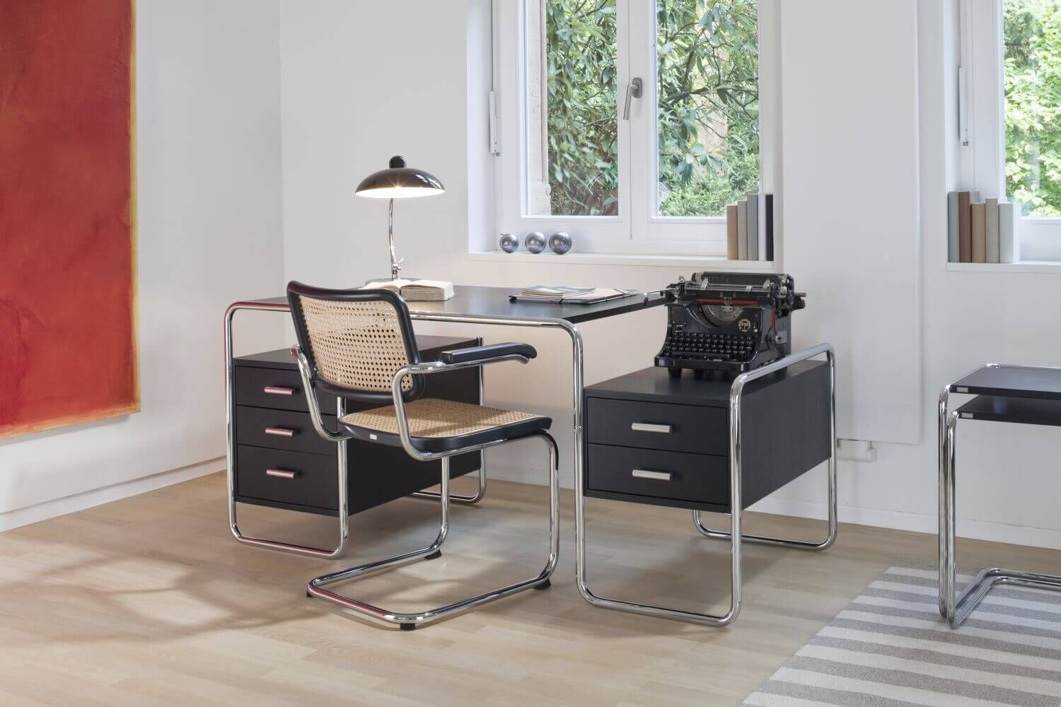 Minimalistisches Büro mit ergonomischem Chromstuhl, Schreibtisch und Schreibmaschine vor einem Fenster.