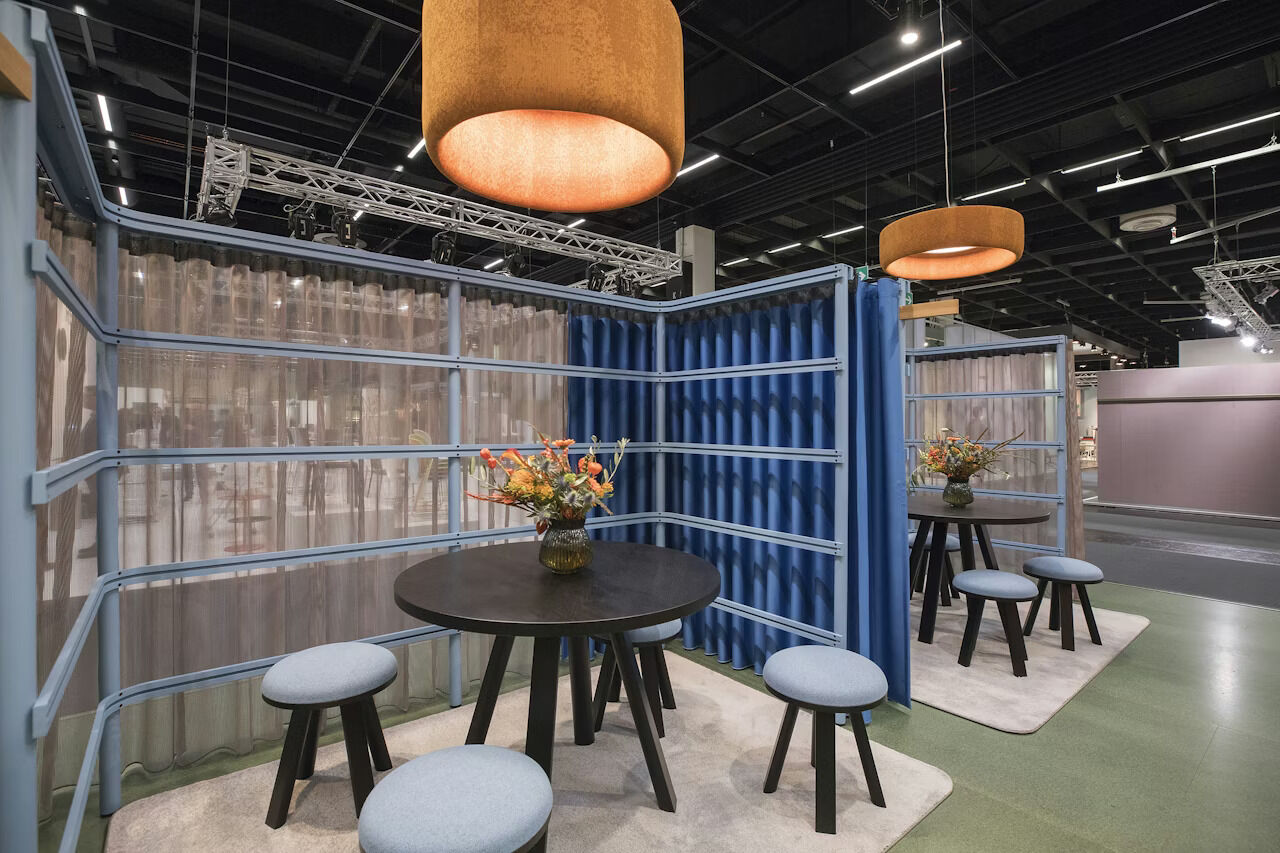 Modernes Bürodesign mit runden Tischen, Hockern und Pendelleuchten in einem Messe-Setup.