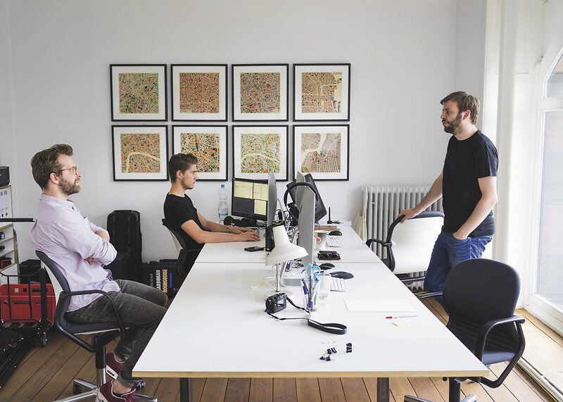 Drei Männer arbeiten in einem modernen Büro mit ergonomischen Stühlen und Computern unter Wandkunst.