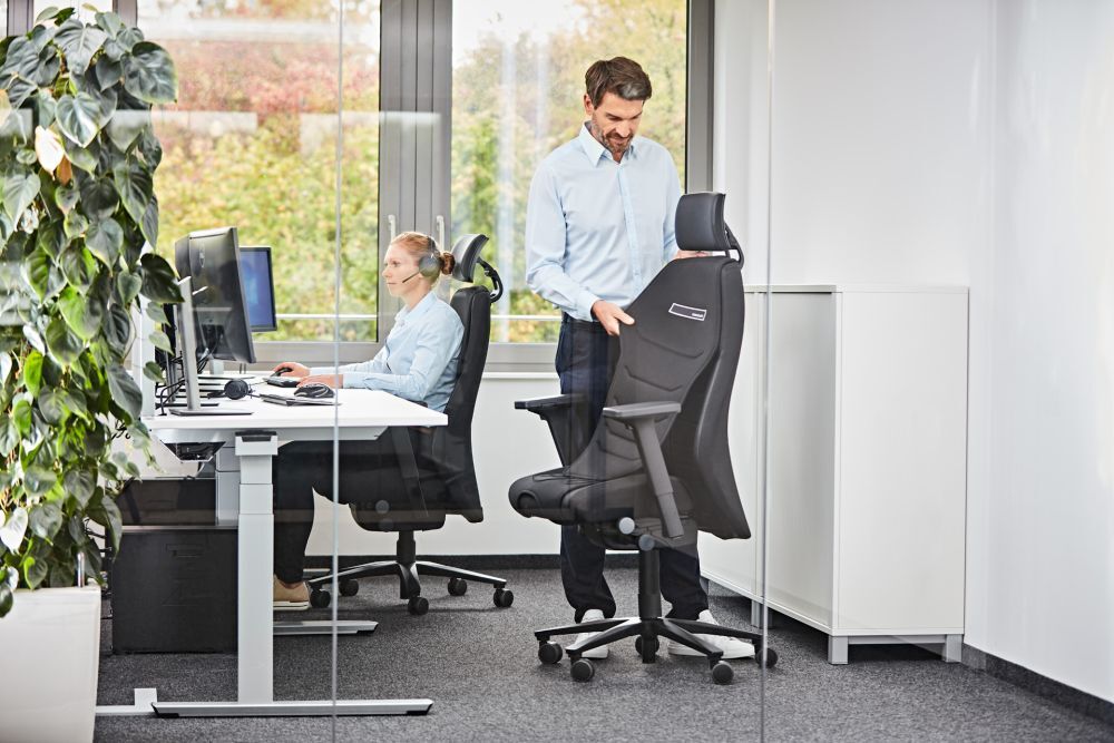 Mann und Frau in einem modernen Büro mit ergonomischen Stühlen, die für dynamisches Sitzen gestaltet sind.