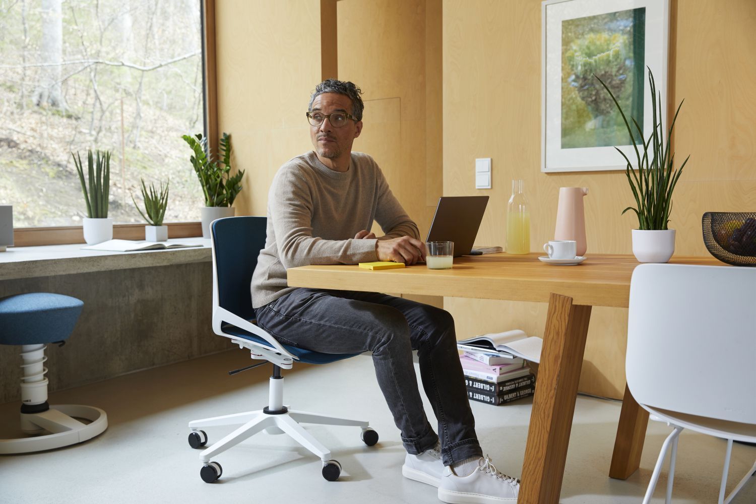 Mann sitzt am Tisch mit Laptop, umgeben von Pflanzen, in einem modernen, hellen Büro.