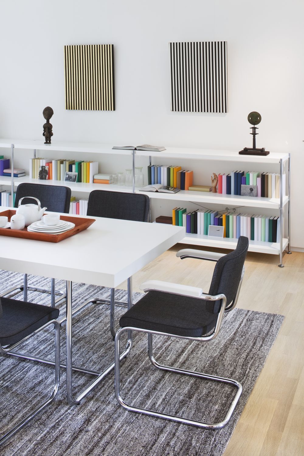 Moderner Büroraum mit stilvollen ergonomischen Stühlen, einem Tisch, Bücherregalen und minimalistischer Kunst an der Wand.