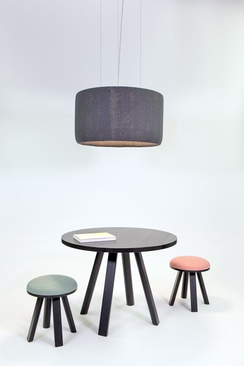 Runder schwarzer Tisch mit zwei bunten Hockern und einer großen, hängenden Lampe darüber.