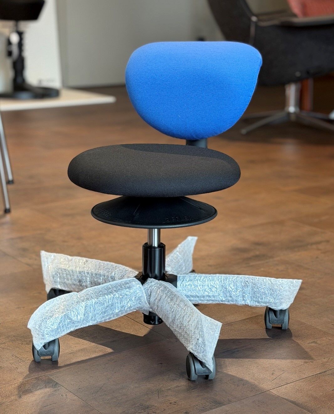Ergonomischer Bürostuhl mit blauer Rückenlehne, schwarzem Sitz und mit Schaumstoff umwickelten Rollen.