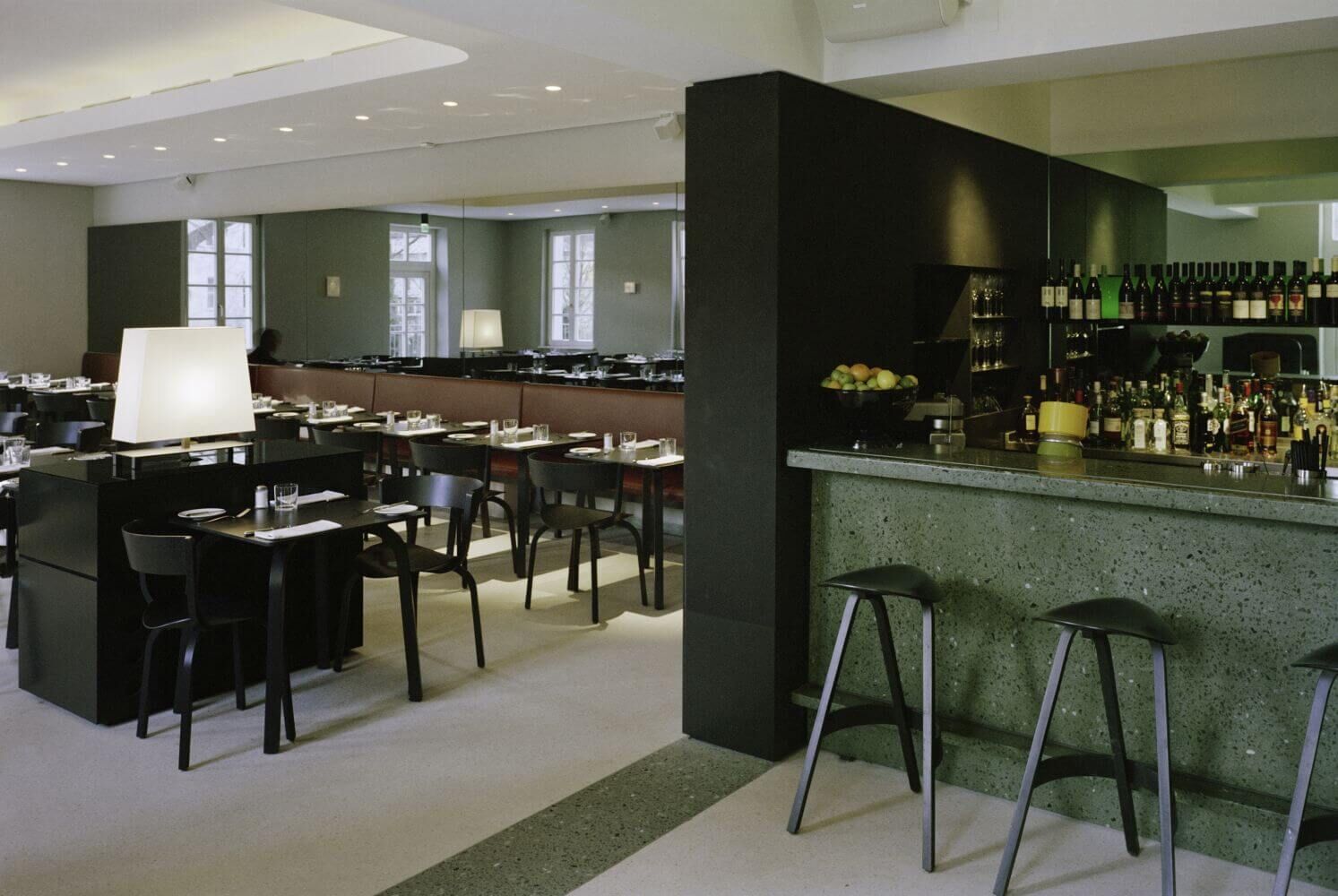 Elegante Restaurant-Bar mit schwarzem Mobiliar, grünem Tresen und moderner Beleuchtung, stilvoll gedeckt.