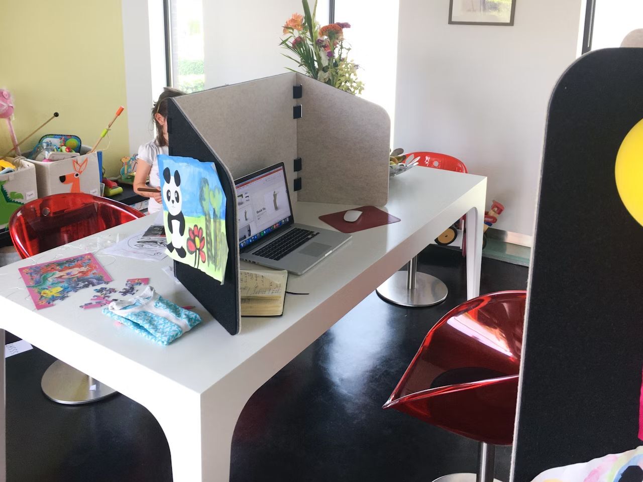 Heller Raum mit weißem Tisch, Laptops, roten Stühlen und Kinderzeichnungen als Dekoration.