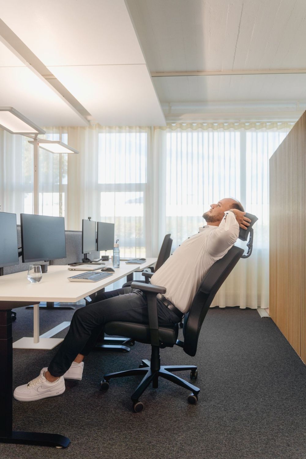 Mann entspannt in ergonomischem Bürostuhl am Schreibtisch mit mehreren Monitoren in modernem Büro.