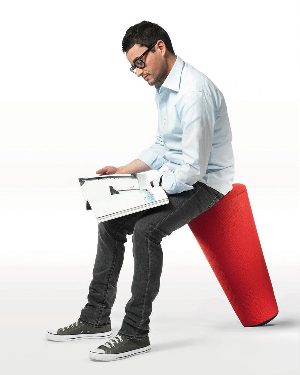 Person sitzt auf einem roten Kipp-Hocker und liest ein Magazin, fördert dynamisches Sitzen.