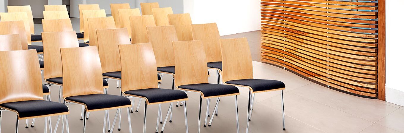 Reihe von modernen Holzstühlen mit schwarzen Polstern vor einer dekorativen Holzwand.