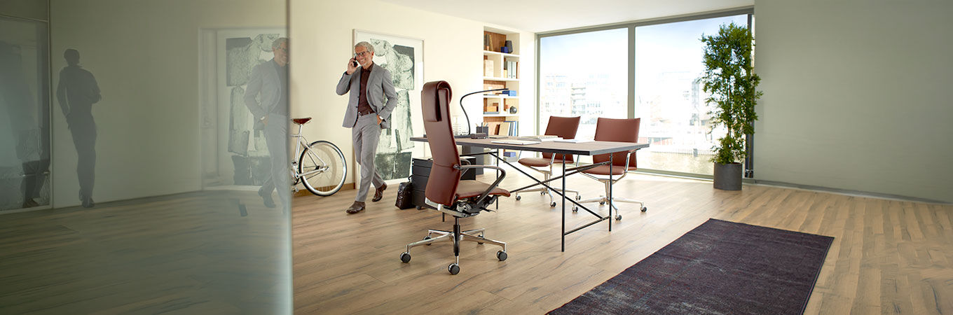 Mann telefoniert in modernem Büro, hochwertige ergonomische Stühle und Schreibtisch im Vordergrund.