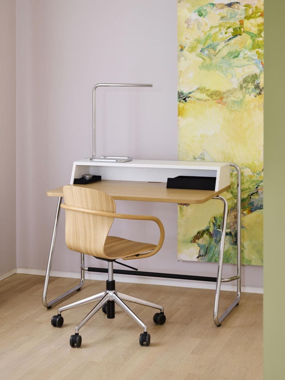 Moderner Schreibtisch mit ergonomischem Bürostuhl aus Holz, Metallrahmen und minimalistischer Tischlampe vor abstraktem Kunstwerk.