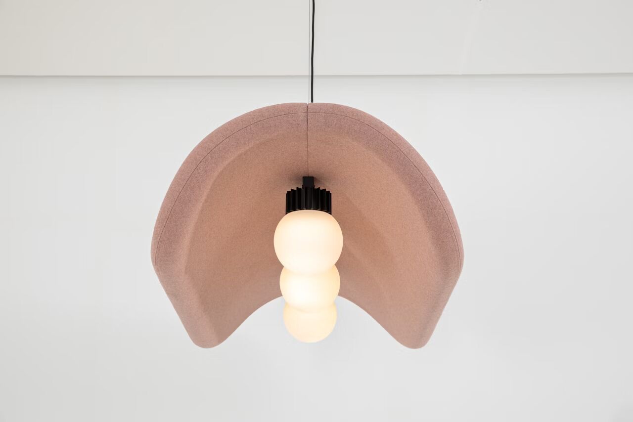 Moderne Hängelampe mit drei weißen Glühbirnen und rosafarbener, gebogener Stoffabdeckung an der Decke.