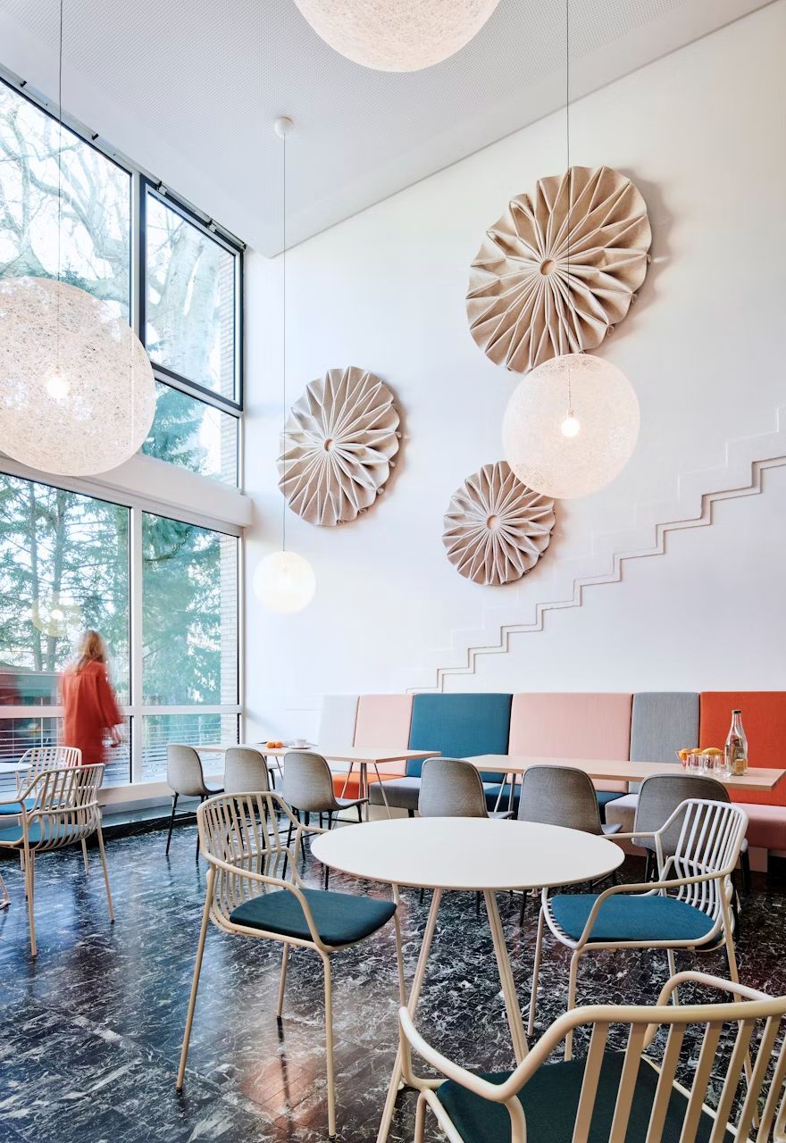 Modernes Café mit stilvollen Stühlen, großen Fenstern und dekorativer Kunst an der Wand. Eine Person geht vorbei.