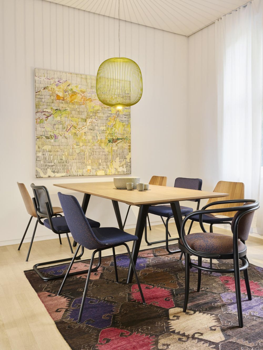 Moderner Essbereich mit Holztisch, bunten Stühlen, buntem Teppich und abstraktem Wandbild unter hängender Lampe.
