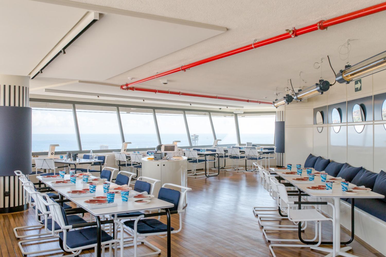 Heller Konferenzraum mit Panoramafenstern, modernen Stühlen und gedeckten Tischen mit blau-weißen Gläsern.