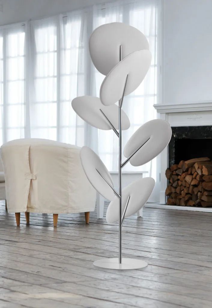 Moderner weißer Raumtrenner in Blattoptik neben einem weißen Sessel in einem eleganten Wohnzimmer.