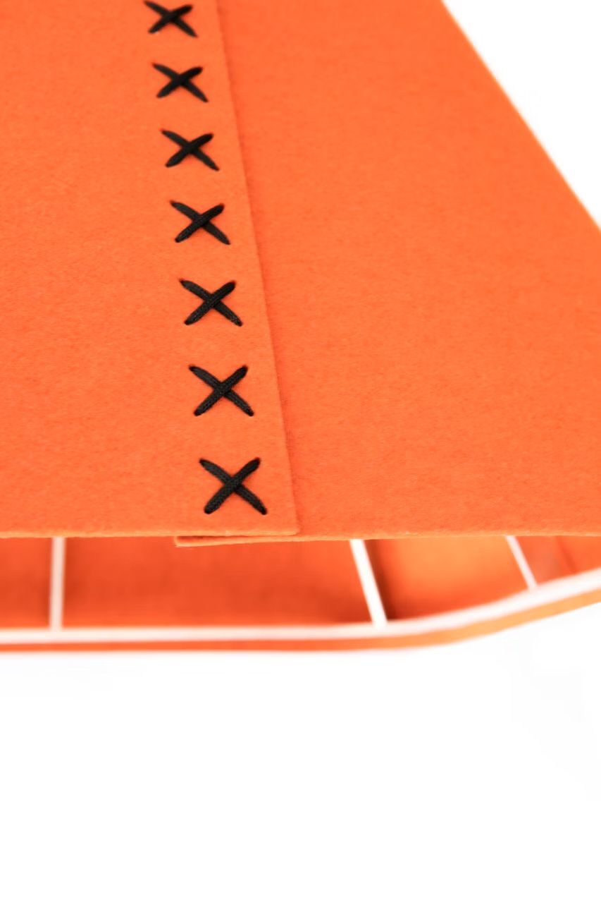 Nahaufnahme eines orangefarbenen Stoffes mit schwarzen Kreuzstichen und mehreren Fächern darunter.