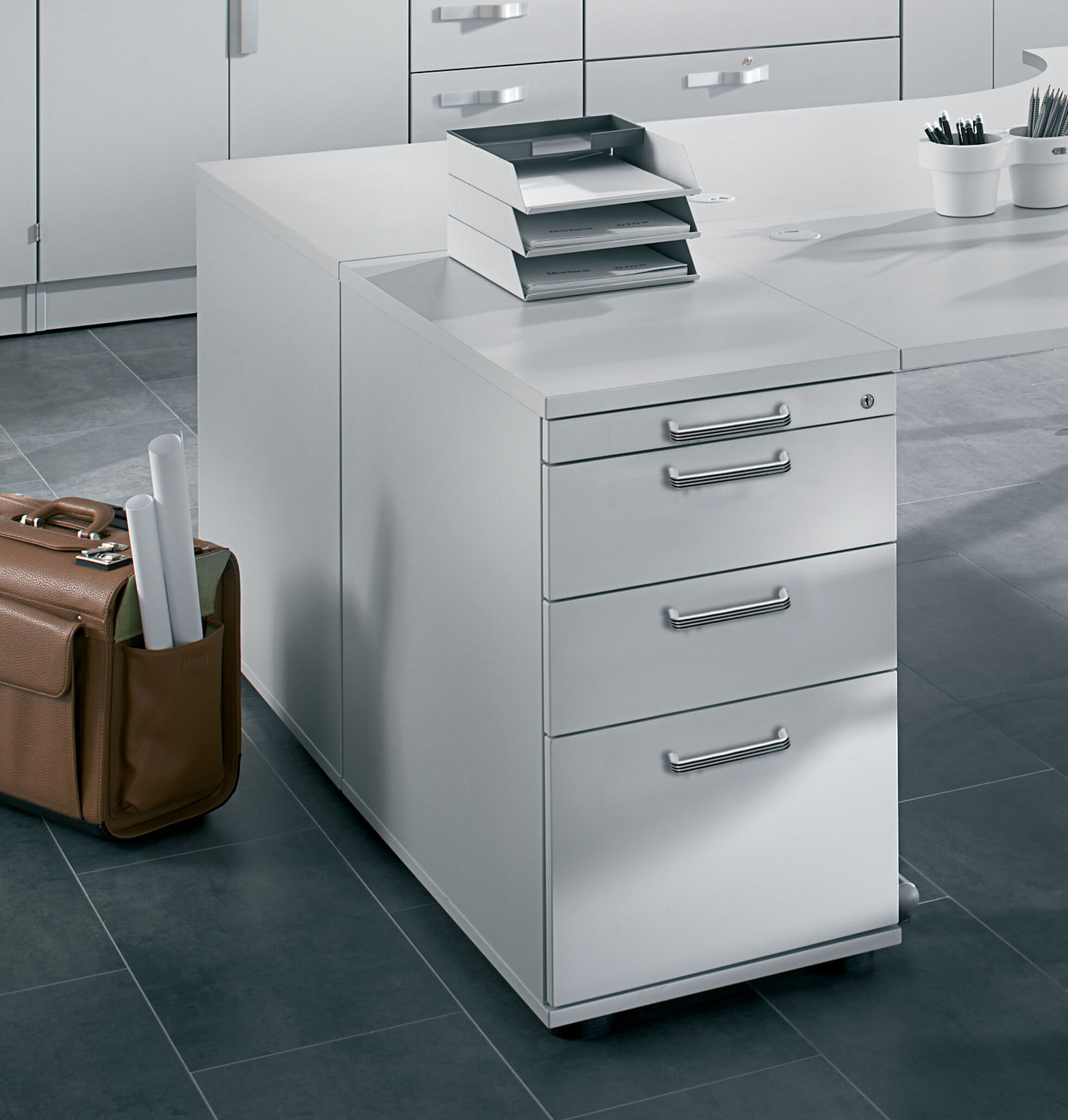 Moderner Büroschrank mit vier Schubladen, eine Aktentasche und Papierablage auf einem grauen Fliesenboden.