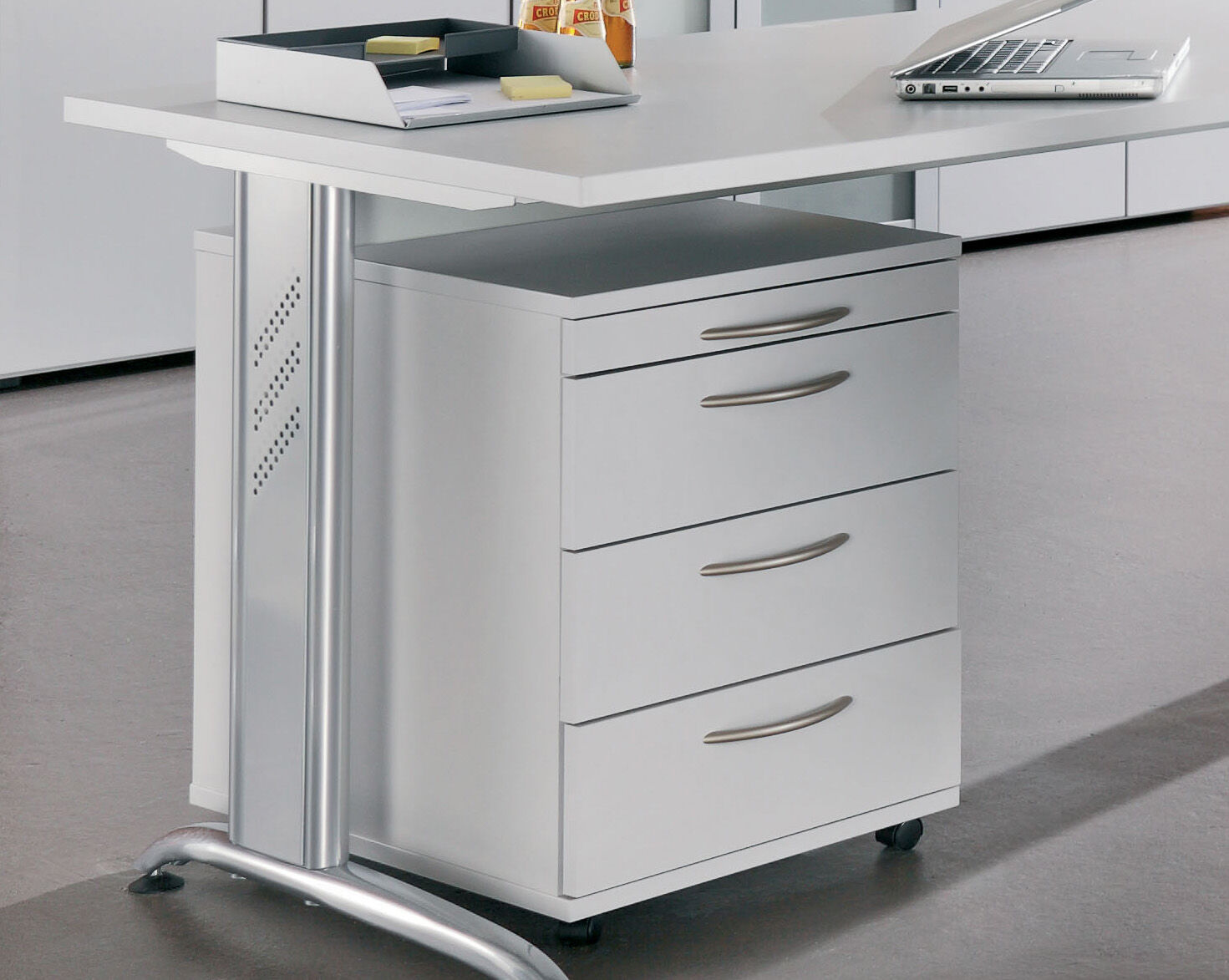 Moderner weißer Schreibtisch mit vier Schubladen, Laptop und Ablage für Büroutensilien, geeignet für ergonomisches Arbeiten.