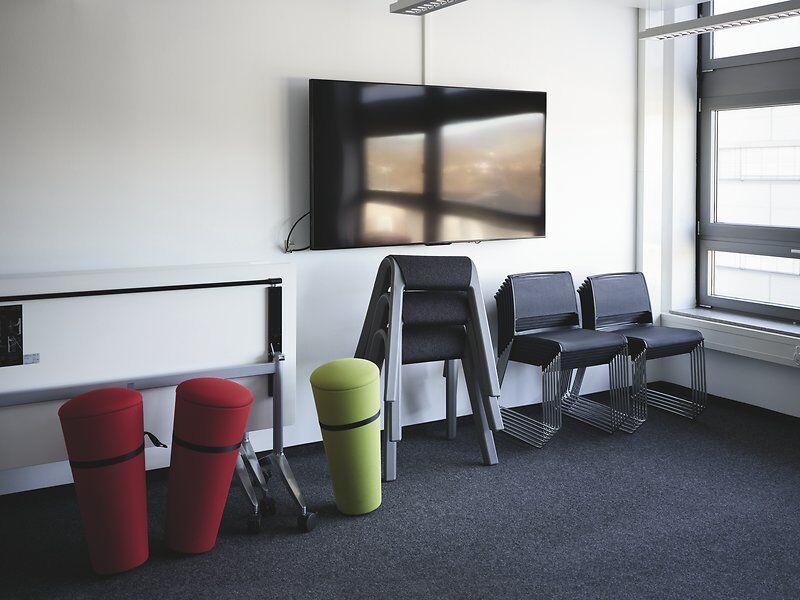 Moderner Büroraum mit bunten ergonomischen Hocker, gestapelten Stühlen und einem großen Flachbildfernseher.