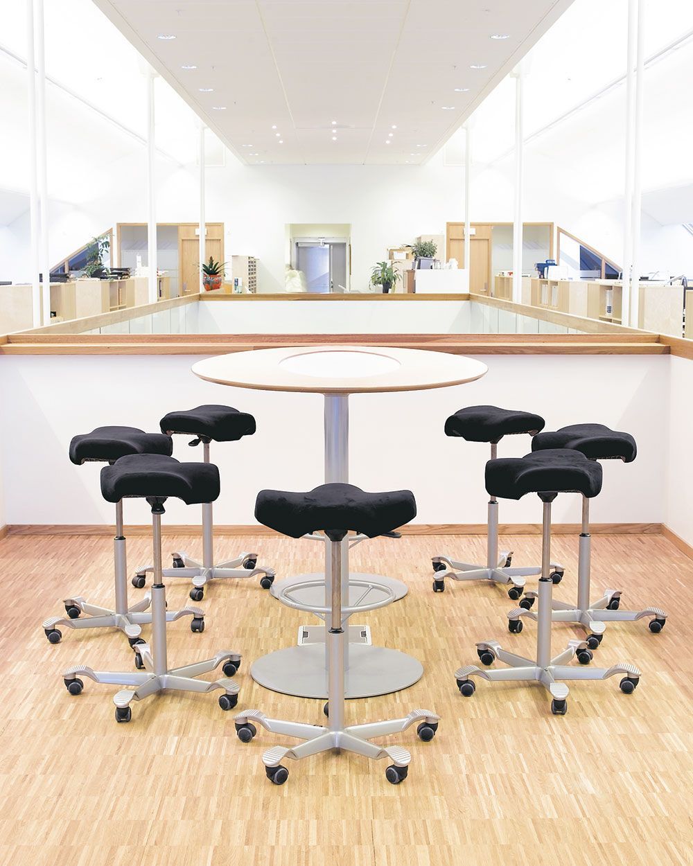 Moderne ergonomische Bürohocker um einen Stehtisch in einem hellen Büroumgebung, betont dynamisches Sitzen.