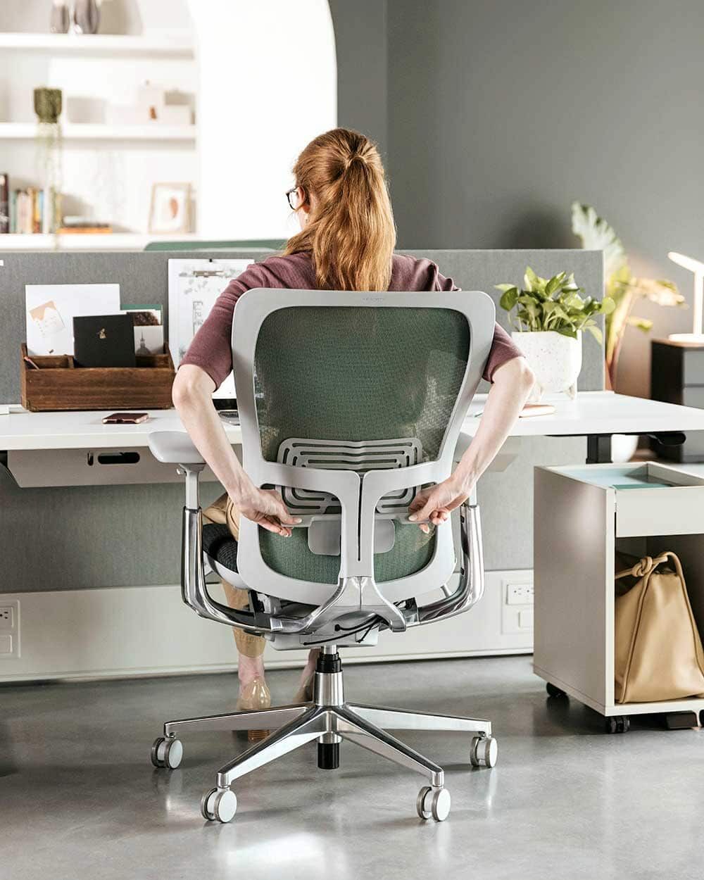 Frau sitzt auf ergonomischem Stuhl und justiert Rückenlehne, betont gesundes, dynamisches Sitzen im modernen Büro.