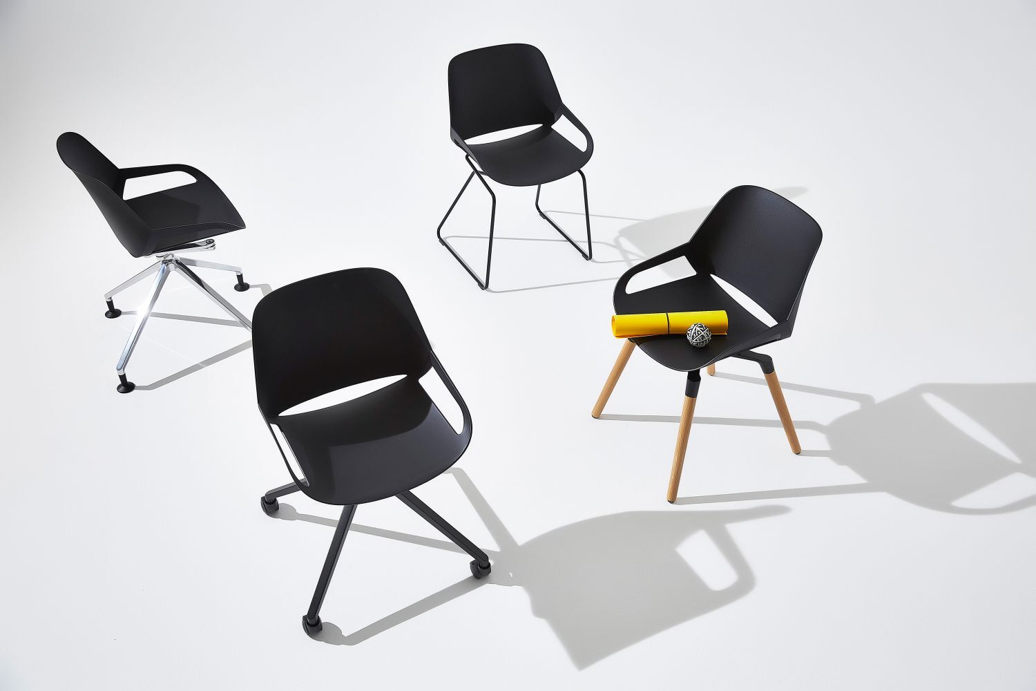 Vier schwarze ergonomische Bürostühle mit unterschiedlichen Gestellen auf einem weißen Hintergrund, einer mit gelbem Stift und Ball.