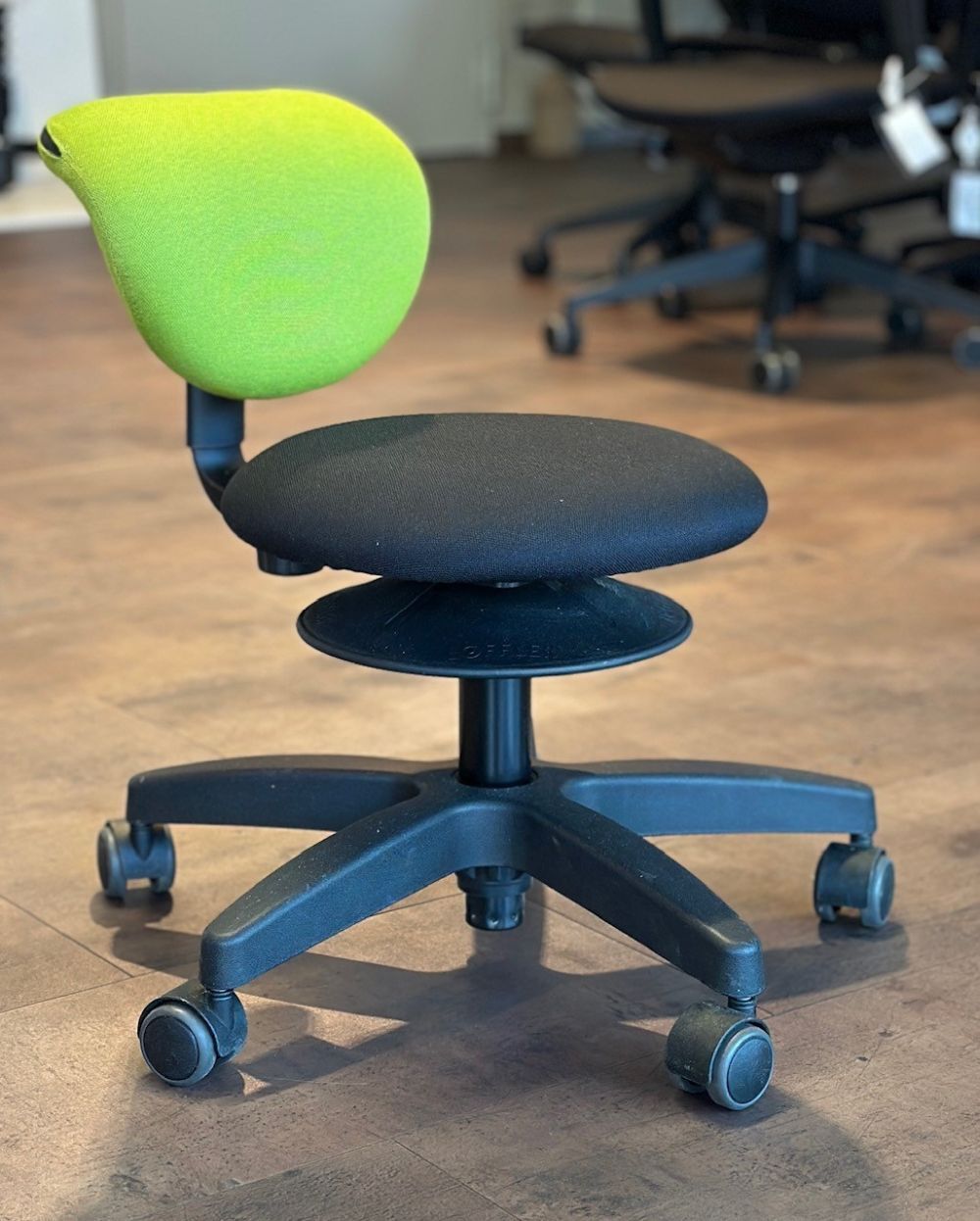 Ergonomischer Bürostuhl mit schwarzem Sitz und grüner Rückenlehne, ideal für dynamisches Sitzen am Arbeitsplatz.