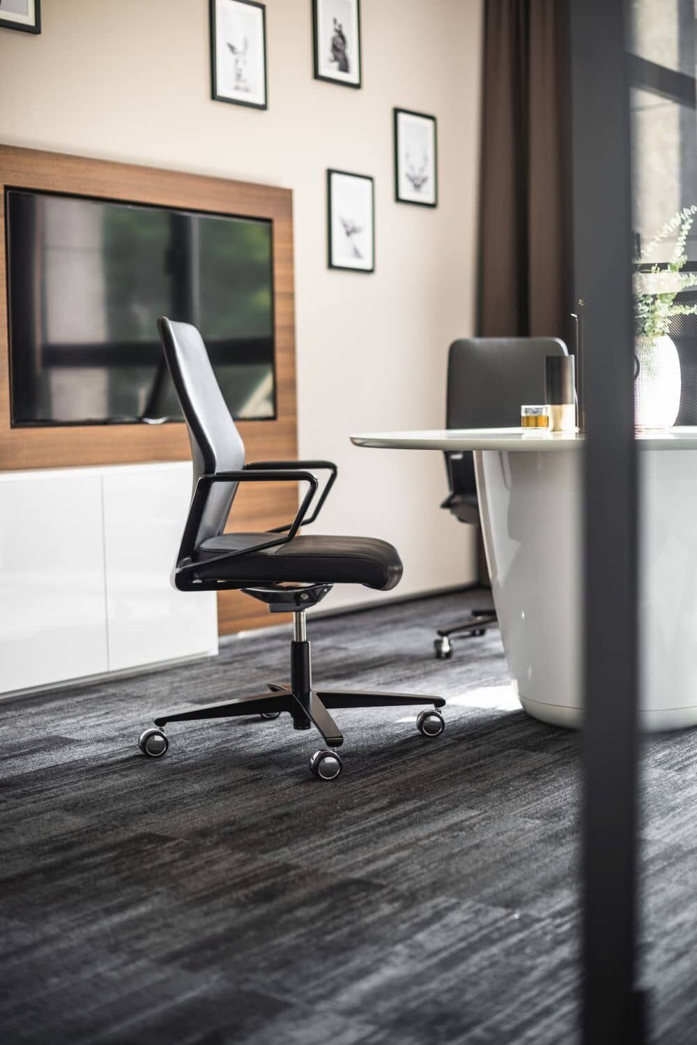 Hochwertiger ergonomischer Bürostuhl in modernem Besprechungsraum mit dunklem Teppich und minimalistischer Wanddekoration.
