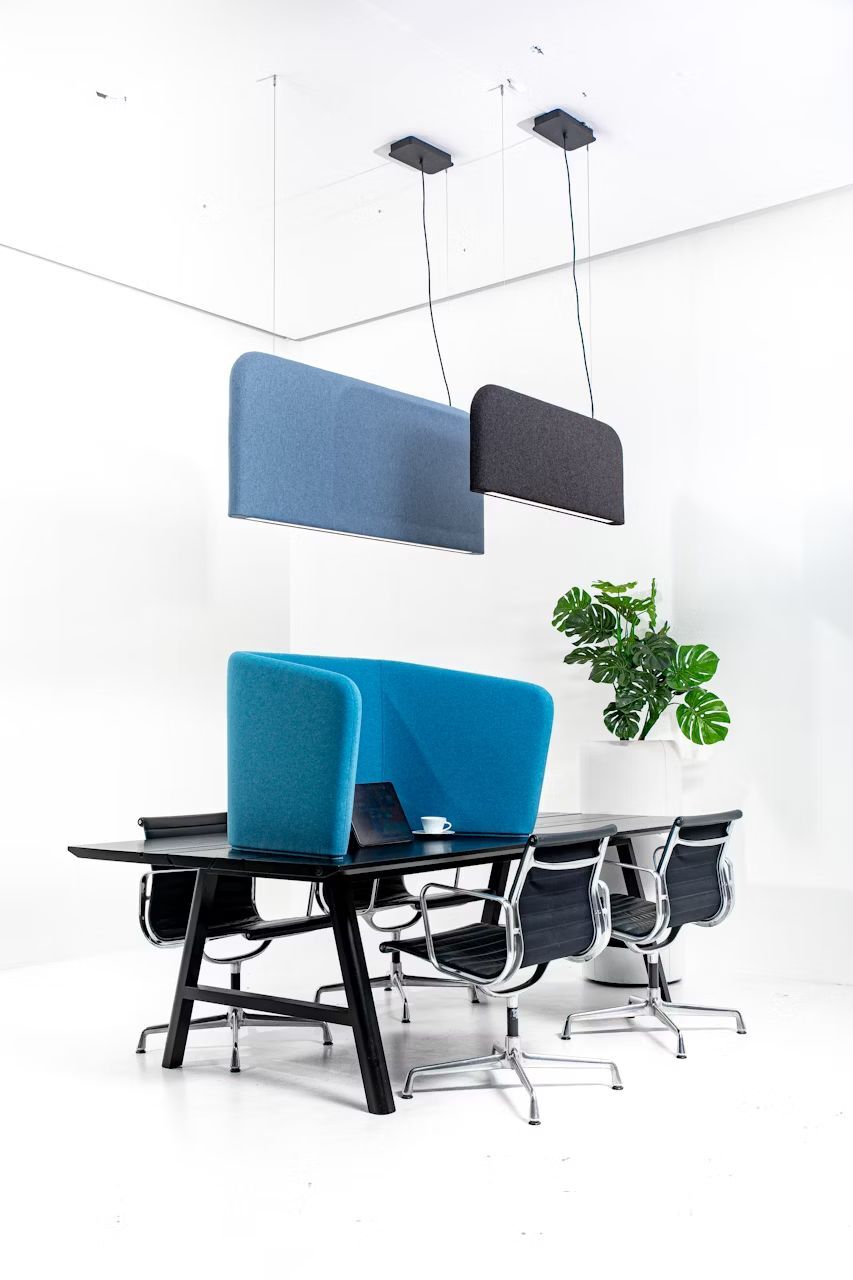Moderner Besprechungstisch mit ergonomischen Stühlen, blauen Trennwänden und Hängelampen in einem hellen Büro.