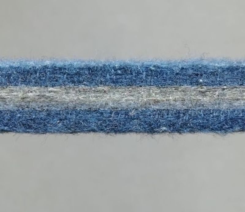 Detailaufnahme eines blauen Filzstreifens mit einem grauen Streifen in der Mitte auf grauem Hintergrund.
