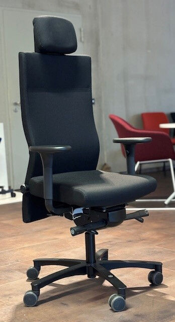 Ergonomischer Bürostuhl mit hoher Rückenlehne und Kopfstütze auf Holzboden, fördert dynamisches Sitzen.