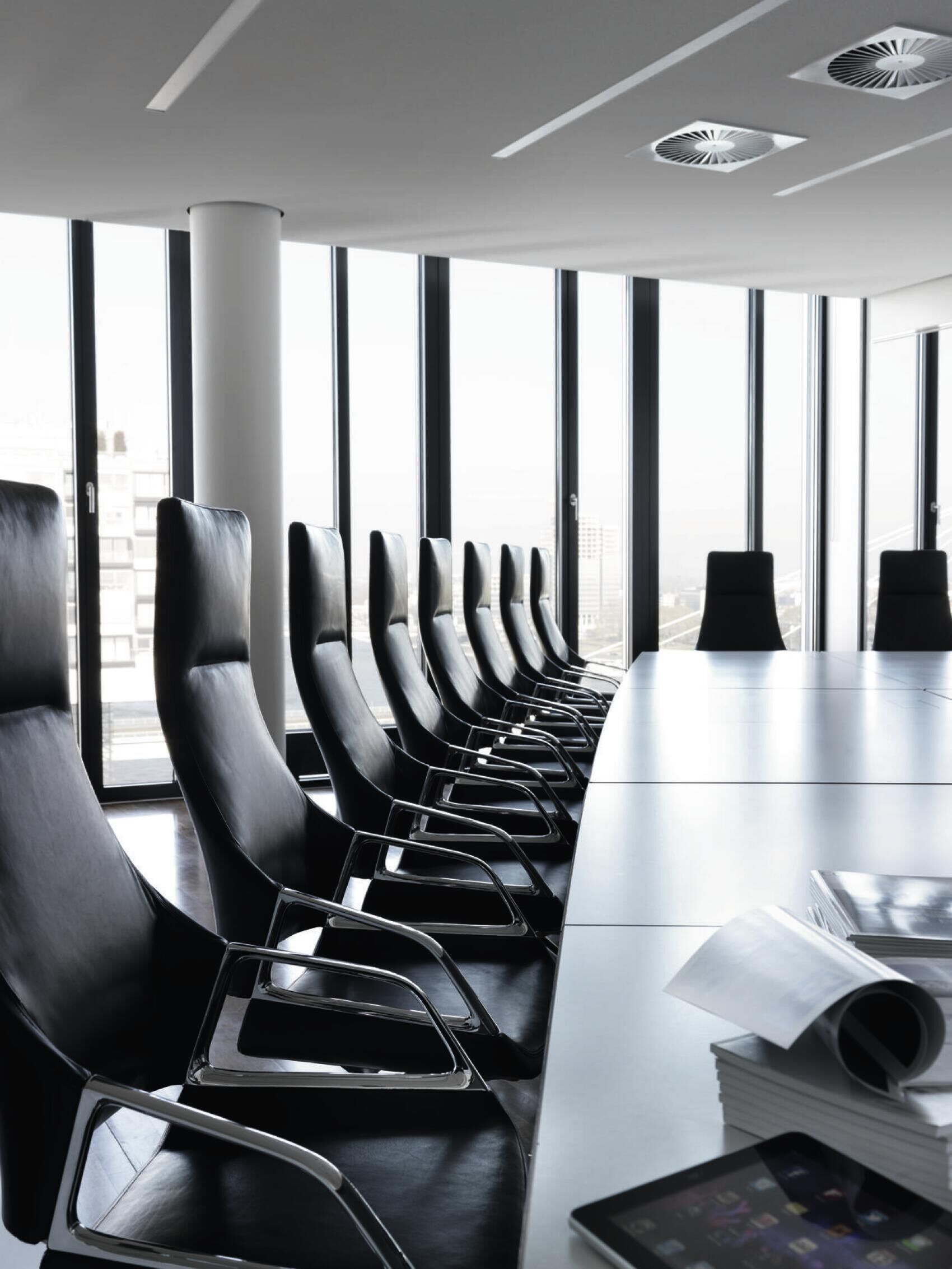 Moderner Konferenzraum mit eleganten schwarzen Bürostühlen und einem großen Tisch, umgeben von großen Fenstern.