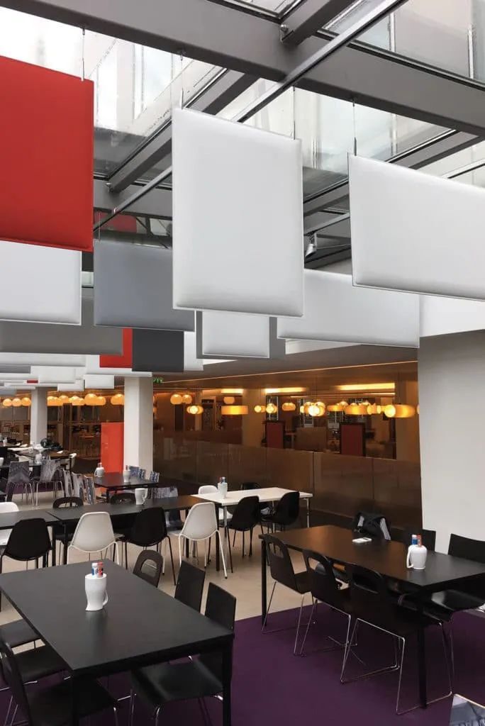 Ein modernes Café mit schwarzen und weißen Tischen, stilvollen Lampen und schallabsorbierenden Paneelen an der Decke.