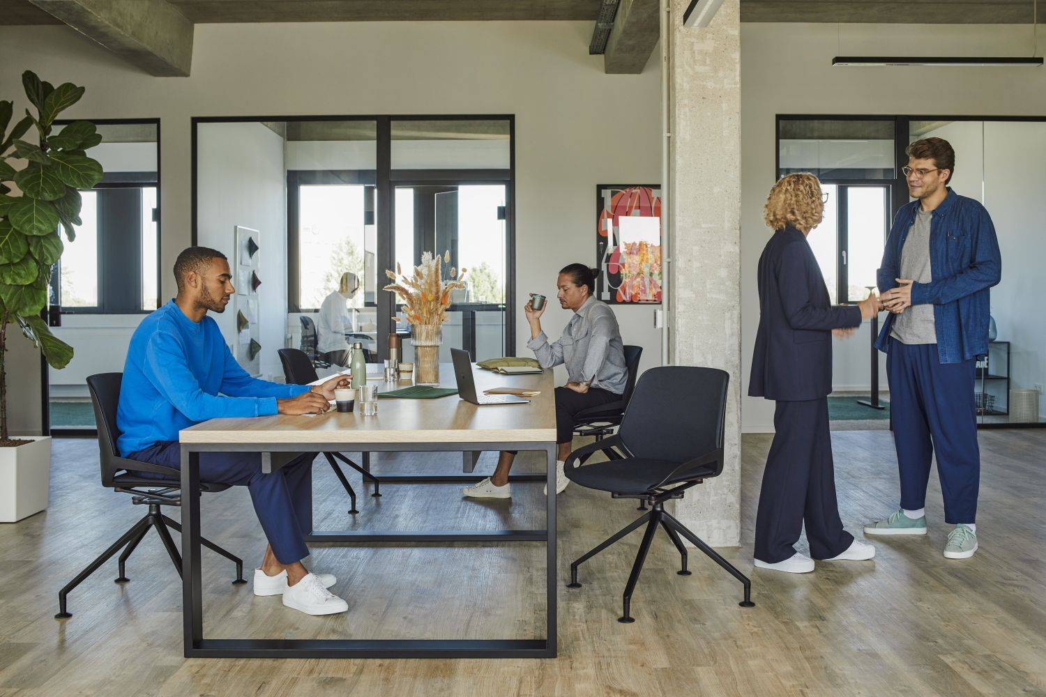 Mitarbeiter in modernem Büro mit ergonomischen Stühlen; zwei Personen unterhalten sich, andere arbeiten am Tisch.