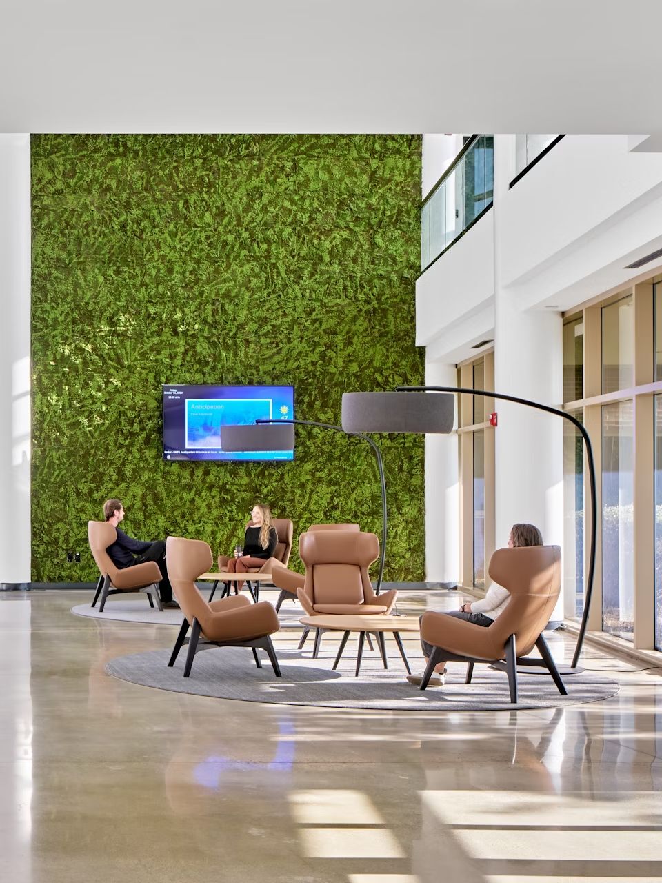 Moderne Lobby mit ergonomischen Sesseln, grüne Mooswand und großem Bildschirm, ideal für dynamisches Sitzen.