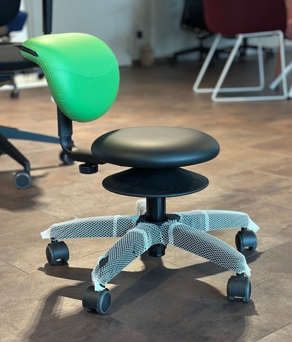 Ergonomischer Bürostuhl mit grünem Rücken, schwarzem Sitz und Netzpolsterung auf den Rollen.