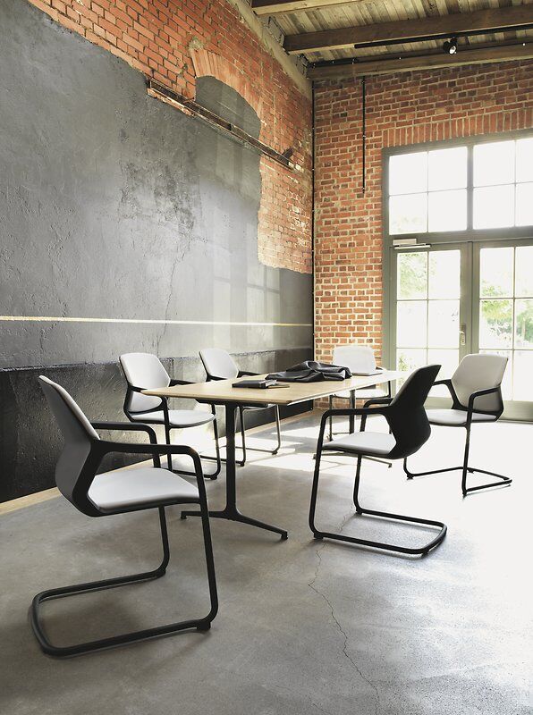 Moderne Besprechungsraum mit ergonomischen Stühlen und Holztisch, Betonboden und Ziegelwänden in heller Loft-Atmosphäre.