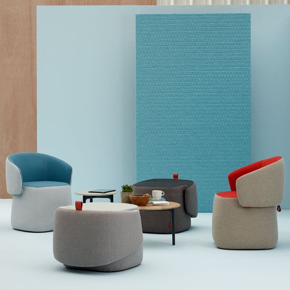 Vier ergonomische, bunte Lounge-Sessel und Tische in modernem Büro-Stil vor pastellblauer Trennwand.