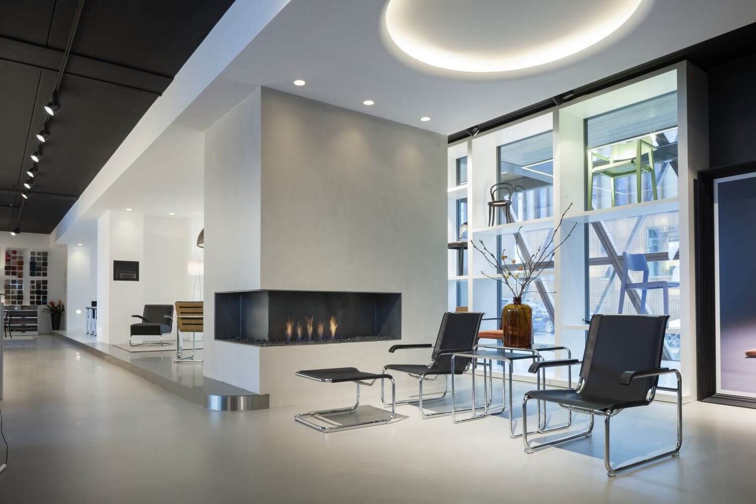Modernes Büro mit ergonomischen Stühlen, Kamin und großer Fensterfront, die einen hellen, einladenden Raum schafft.